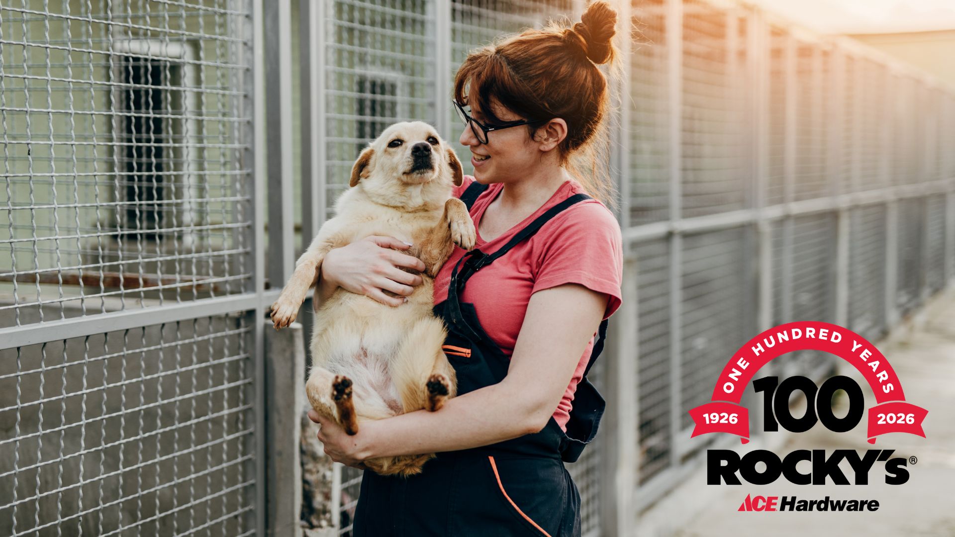 A pet shelter employee holding a rescue dog at a pet shelter. The Rocky's Ace Hardware 100-Year Anniversary logo is in the lower right corner.